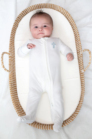 Baby in a white outfit with a cross design, lying in a woven basket on a white background