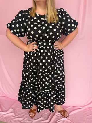 Person wearing a black dress with white polka dots against a pink background