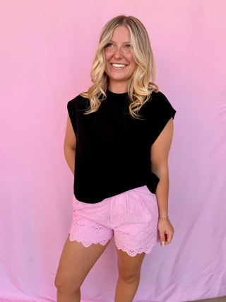 Woman wearing a black top and pink shorts against a pink background