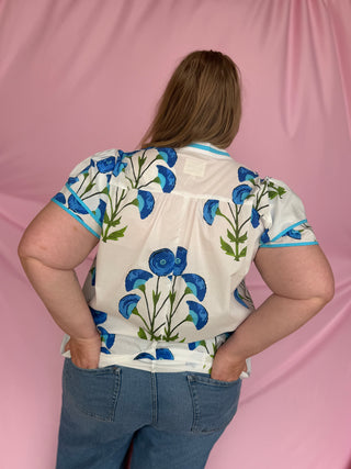 Person wearing a floral blouse with blue flowers on a pink background