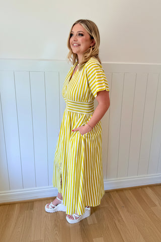Woman wearing a yellow striped dress and colorful headpiece indoors.