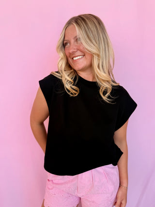 Woman wearing a black top and pink pants against a pink background