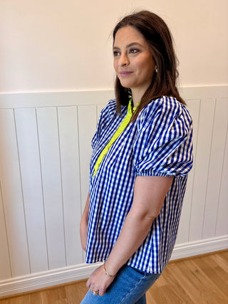 Woman wearing a blue and white checkered blouse with a yellow stripe indoors.