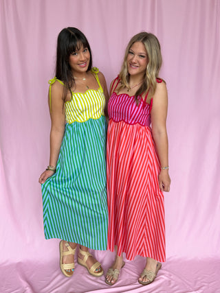 Two women wearing colorful striped dresses against a pink background
