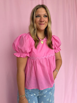 Woman wearing a pink blouse with puffed sleeves against a pink background