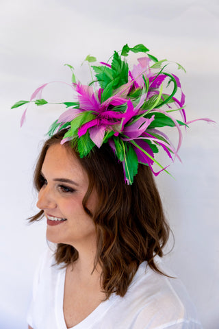 Woman wearing a decorative headpiece with green and pink feathers on a white background