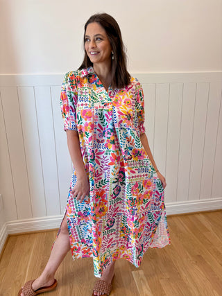 Woman wearing a colorful floral dress standing in a room with wooden flooring and white paneled walls.
