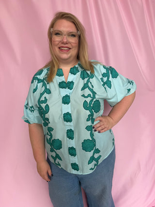 Woman wearing a light blue dress with green floral patterns on a pink background
