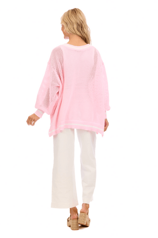 Woman wearing a pink oversized sweater and white pants on a white background