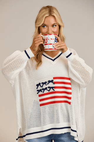 Woman wearing a white sweater with an American flag design, holding a mug.