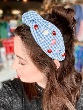 Woman wearing a blue checkered headband with decorative elements in a blurred indoor setting
