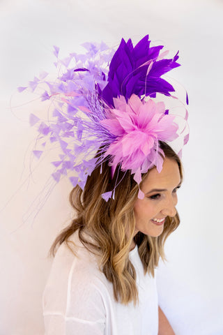 Woman wearing a decorative headpiece with purple and pink feathers against a white background