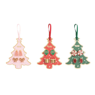 Three Christmas tree-shaped ornaments in pastel pink, coral red, and sage green, each with hanging ribbons and small holiday embellishments, shown on a plain white background.