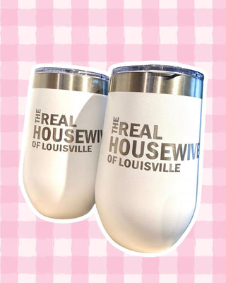 Two white insulated stemless wine tumblers with stainless steel rims and clear lids, printed with the text 'THE REAL HOUSEWIFE OF LOUISVILLE' in dark gray, shown against a pink and white gingham background.