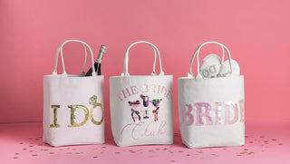 Three white gift bags with 'I DO', 'The Bride Club', and 'Bride' text on a pink background.