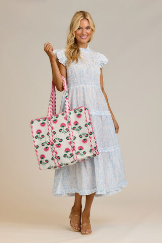 Woman holding a floral tote bag wearing a light blue dress on a beige background