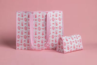 A pink and white patterned fabric organizer pouch with multiple compartments, shown alongside a matching small cylindrical pouch on a solid pink background.