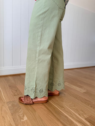 Person wearing light green pants with lace details on a wooden floor.