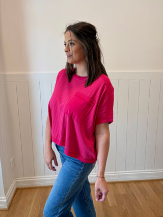 Woman wearing a bright pink t-shirt and blue jeans standing in a room with white paneled walls.