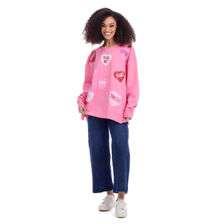 Woman wearing a pink sweatshirt with text and graphics, standing against a white background