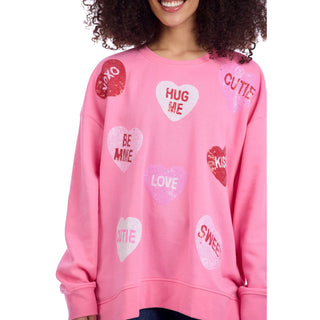 Person wearing a pink sweatshirt with heart-shaped text designs on a white background