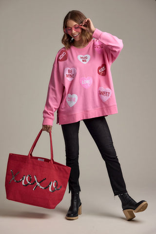 Woman wearing a pink sweatshirt with heart-shaped text and holding a red tote bag with 'XOXO' on a neutral background