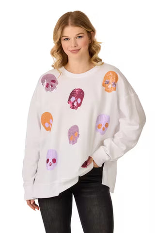 A woman wearing a white crewneck sweatshirt with colorful sequined skull patches, paired with black jeans, against a plain white background.