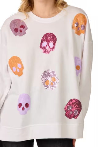 A white crewneck sweatshirt featuring an all-over sequined skull pattern in various colors including pink, purple, orange, and yellow, worn by a model.