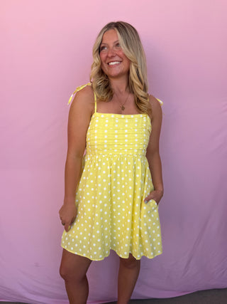 Woman wearing a yellow polka dot dress against a pink background