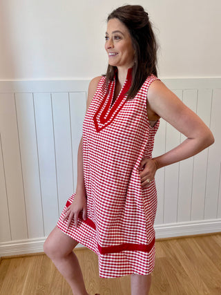 Woman wearing a red and white checkered dress against a white paneled wall.