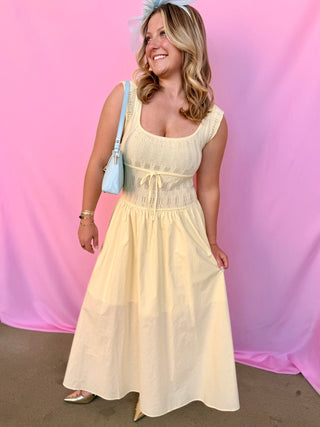 Woman in a light yellow dress standing against a pink curtain