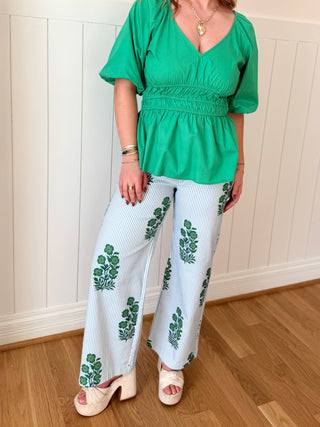 Person wearing a green top and white pants with green patterns on a wooden floor.