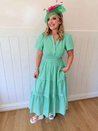 Woman wearing a green dress with a matching hat against a white paneled wall.