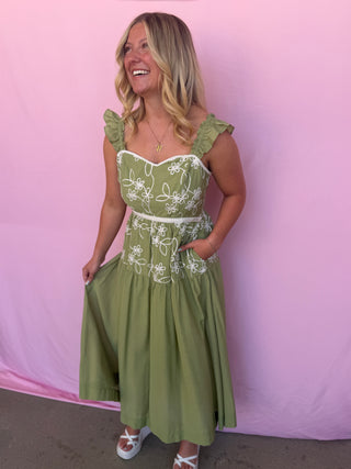 Woman wearing a green dress with white embroidery against a pink background