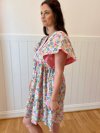 Woman wearing a floral dress standing against a white paneled wall.
