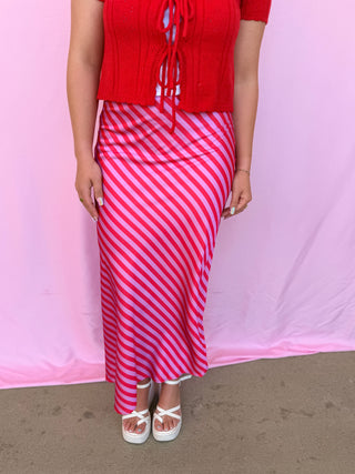 Person wearing a red top and pink striped skirt against a pink background