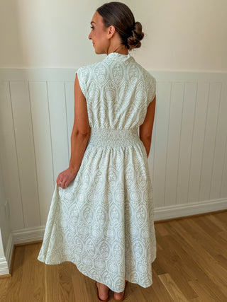 Woman wearing a white lace dress standing against a white paneled wall.