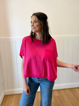 Woman wearing a bright pink shirt and blue jeans standing in a room with white paneled walls.