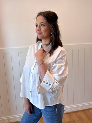 Woman wearing a white blouse with rolled-up sleeves against a white wall.
