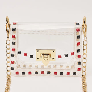 White handbag with gold chain strap and black and red studded details on a white background