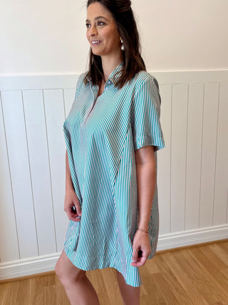 Woman wearing a blue and white striped dress standing against a white paneled wall.