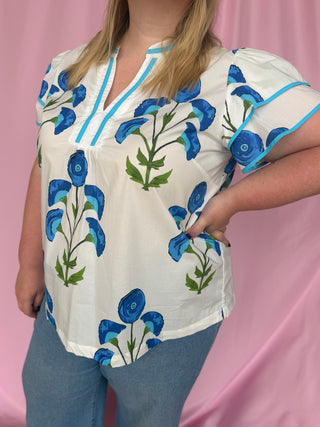Person wearing a white blouse with blue floral patterns on a pink background