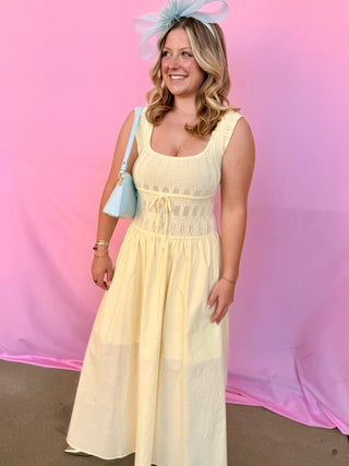 Woman in a light yellow dress with a blue handbag against a pink background
