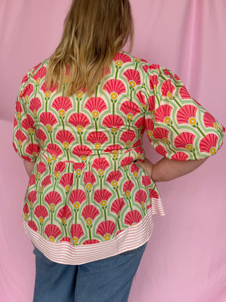 Person wearing a colorful patterned blouse with a pink background