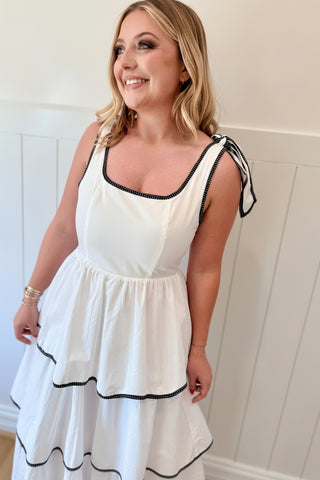 Woman wearing a white dress with black trim against a white wall.