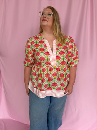 Person wearing a patterned top and jeans against a pink background