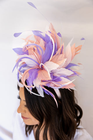 Woman wearing a decorative headpiece with pink and purple feathers on a plain background