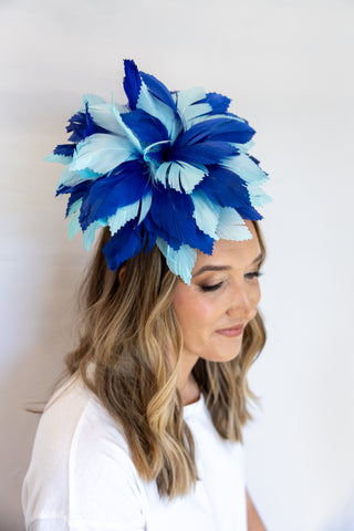 Woman wearing a large blue and white feathered headpiece against a white background