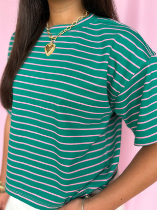 Green and white striped shirt worn by a person with a pink background
