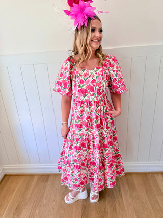 Woman wearing a pink floral dress and headband against a white paneled wall.